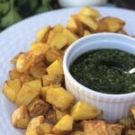 Knusprige Patatas Bravas mit grüner Mojo-Sauce auf einem weißen Teller, daneben frische Petersilie.