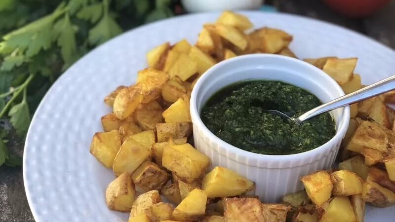 Knusprige Patatas Bravas mit grüner Mojo-Sauce auf einem weißen Teller, daneben frische Petersilie.