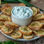 Selbstgemachter Tzatziki-Dip mit frischer Gurke und Dill, serviert mit knusprigen Brotchips aus Brötchen – angerichtet auf einem weißen Teller